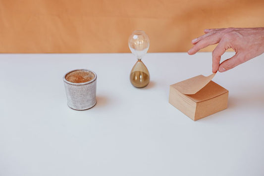 A minimalist desk setup featuring an hourglass, coffee cup, and notepad for time management inspiration.