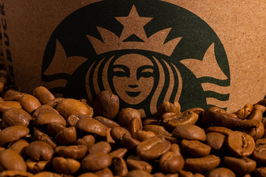 A detailed image of roasted coffee beans placed in front of a cardboard cup featuring a green logo.