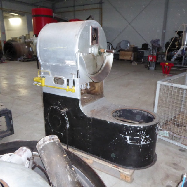 A large industrial coffee roaster unit with a silver cylindrical upper section, black lower body, and yellow safety handles, photographed in a warehouse or workshop setting.